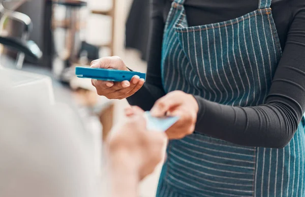 Closeup of a clerk accepting a credit card payment from a customer in a cafe or store. Hands of woman using card machine reader while taking money for a purchase transaction from a man in a shop.