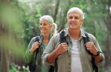 A mature caucasian couple out for a hike together. Senior man and woman smiling and walking in a forest in nature.