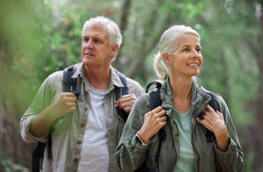 A mature caucasian couple out for a hike together. Senior man and woman smiling and walking in a forest in nature.