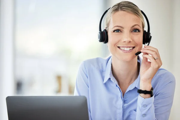 Portrait of young caucasian female call centre agent talking on headset while working on computer in an office. Confident and happy businesswoman consulting and operating a helpdesk for customer sale.