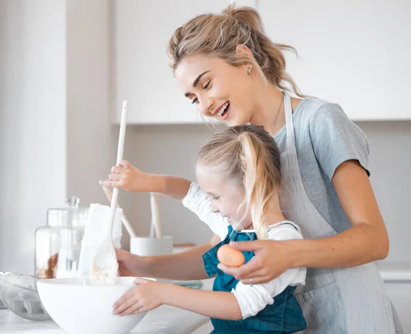 Mother helping her daughter bake. Happy woman holding an egg helping her child bake. Little girl mixing a bowl of batter. Small child bonding with her mother and cooking together.Happy family baking.