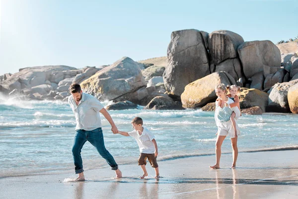 陽気な白人の家族がビーチを歩いています 夏休みにビーチで楽しい2人の子供を持つ幸せな家族 明るい夏の日に両親と一緒に休暇を楽しむ子供たち — ストック写真