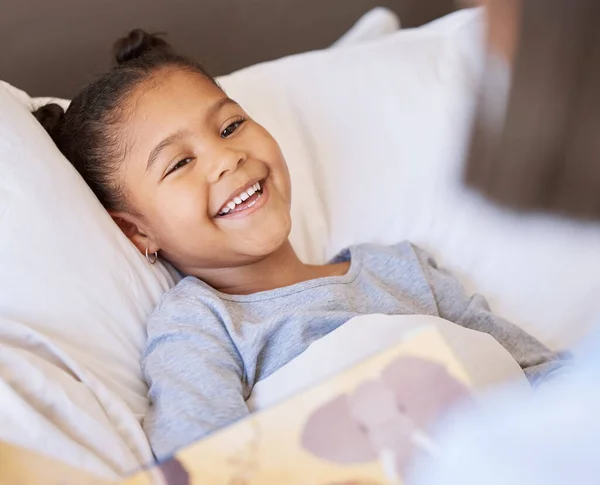Mother reading storybook to daughter at bedtime. Adorable little girl laughing while lying in bed and enjoying a story while being tucked in by mom.