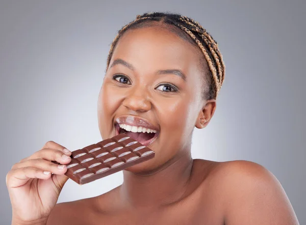 Heavens made of chocolate. Studio shot of an attractive young woman eating a slab of chocolate against a grey background