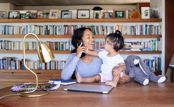 Mother working from home phone call with baby. Hispanic woman making call on smartphone. Teleworking businesswoman at home with baby. Mother holding a baby working in her study