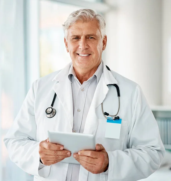 当一个人在医院工作时 成熟的高加索男性专家医生笑着使用数字平板电脑 一位穿着工作服 在诊所的办公室里工作着数码平板电脑的老年人 — 图库照片