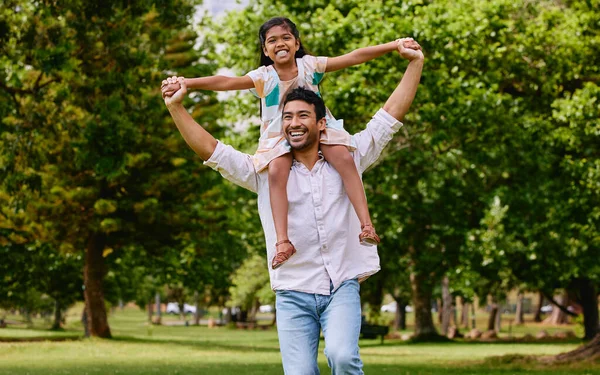 Happy asian single father carrying daughter on his shoulders in the park. Smiling man and child pretending they can fly with their arms outstretched. Single parent bonding with his little girl outsid.