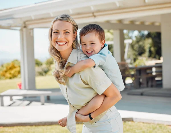 Happy single mother giving her little son a piggyback ride outside in a garden. Smiling caucasian single parent bonding with her adorable child in the backyard. Playful kid enjoying free time with mo.