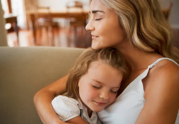 Young loving caucasian mother hugging her little daughter relaxing and sitting on the couch together at home. Innocent carefree girl embracing her mom resting on the couch.