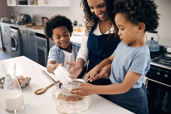 快乐的非洲裔美国家庭在家里的厨房里一起烘焙 两个小男孩一边学习一边很开心地帮助他们的母亲筛选蛋糕配方的配料 很高兴享用甜食 — 图库照片