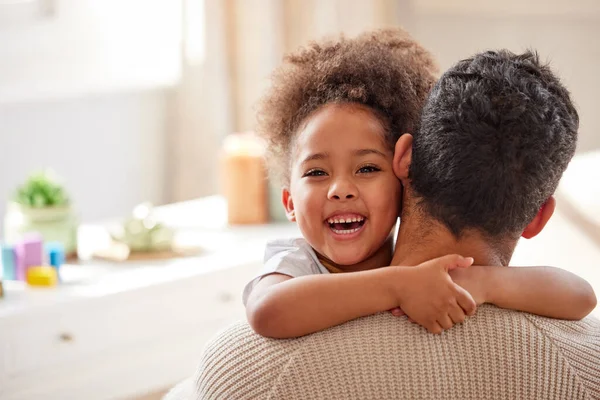Adorable little mixed race girl with curly afro hair smiling and hugging her father at home. Hispanic father bonding and embracing his daughter. Cheerful African American child with her single parent.