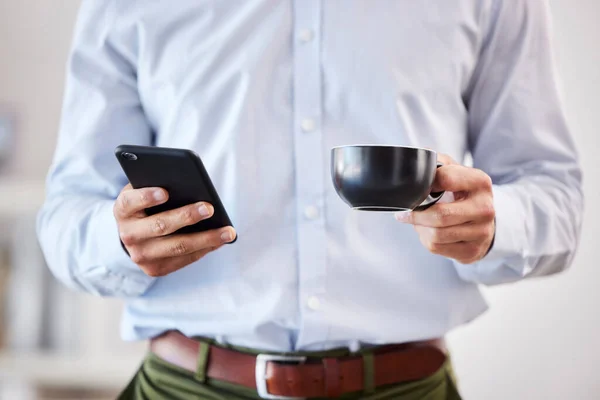 Closeup of male hands holding coffee and smartphone. Businessman using mobile phone to send text, browse social media or use app while on his tea break.