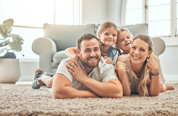 Young family in the living room at home. Portrait of an affectionate and happy family lying on the floor of the lounge. Spending quality time together. A mother, father and two sisters at home.