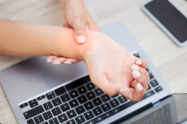 My wrist is bothering me again. Closeup shot of an unrecognisable businesswoman experiencing wrist pain while working on a laptop in an office