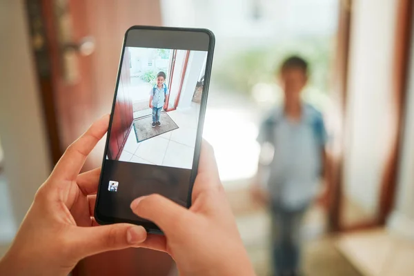 Closeup of mother taking photo of son on first day of school. Hands taking picture on cellphone of kindergarten boy standing by the door and ready to leave home. Proud mom documenting childhood.