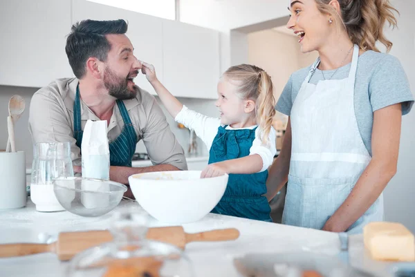 Excited family baking together.Caucasian family playing and baking. Little girl playfully putting flour on her fathers nose. Happy mother and father baking with their daughter