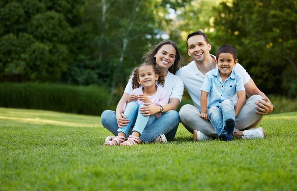 Portrait of carefree mixed race family spending time together at park. Happy parents with son and daughter bonding and having fun outdoors. Young couple sitting with two children sitting on grass.