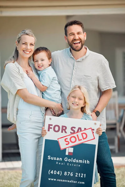 Portrait of happy caucasian family holding for sale and sold sign while relocating and moving in new house. Smiling parents and kids securing homeowner loan for property real estate and home purchase.