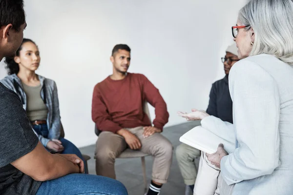 Closeup of a young diverse support group during a meeting with a professional female therapist. Group of employees looking serious during a team counselling session. Mental health in the workplace.