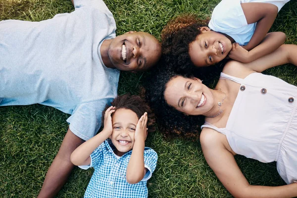 Above view of cheerful african american family lying in a circle. Dad, mom and their two lovely children lying on the grass looking at camera. Little boy and girl having fun with parents at park.