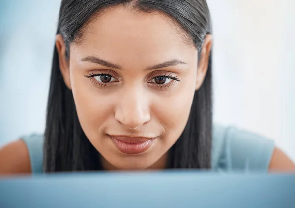 Happy young mixed race businesswoman focused while working on a laptop alone in an office at work. Face of an brunette hispanic female boss sending an email using a laptop.