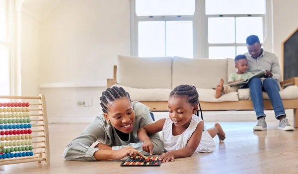 African american girl playing with an abacus and other toys while lying on the floor with her mother. Young daughter bonding with her mom. Smiling woman lying on the floor and playing with child.