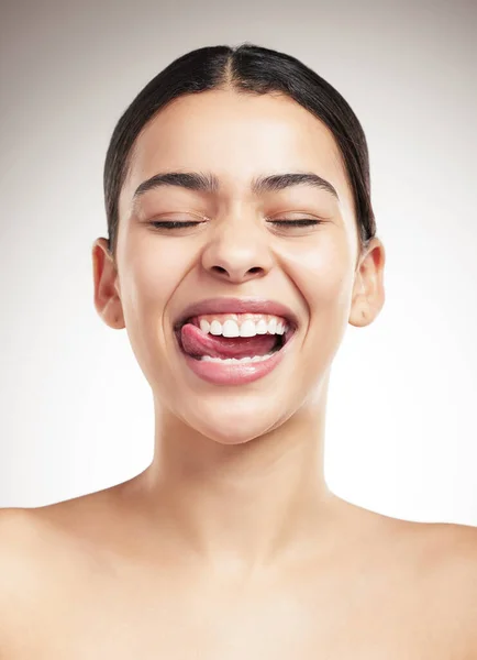 Young joyful mixed race woman sticking out her tongue and posing against a grey studio background. Confident hispanic female smiling while posing against a background.