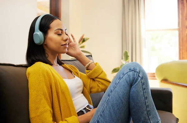 Woman, music and relax with headphones on living room sofa enjoying calm relaxation at home. Young female relaxing on a couch listening to calming audio track at the house for stress relief.