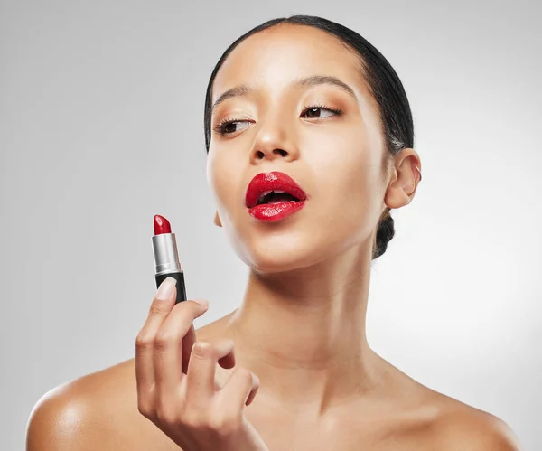 Red lipstick is the beauty equivalent of a shot of espresso. Studio shot of a young woman applying red lipstick against a grey background