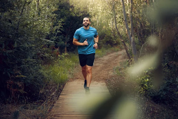 Man, running and fitness on forest path, nature woods bridge or countryside environment for health, wellness or heart health. Smile, happy or sports runner in exercise, training and workout in Canada.