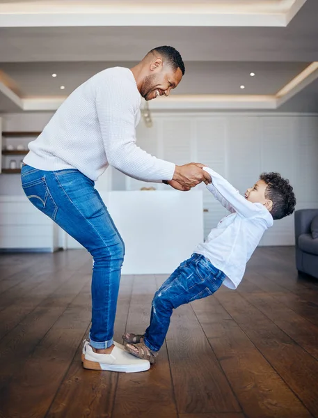 Little boy standing on dads feet and sharing a dance. Playful dad and son having fun together at home. Cheerful man teaching his son to dance.