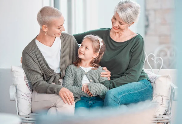 Three generations of females sitting together and looking at each other. Adorable little girl bonding with her mother and grandmother at home.