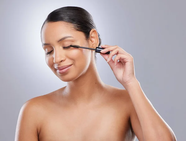 Heres to longer lashes. an attractive young woman standing alone in the studio and applying mascara