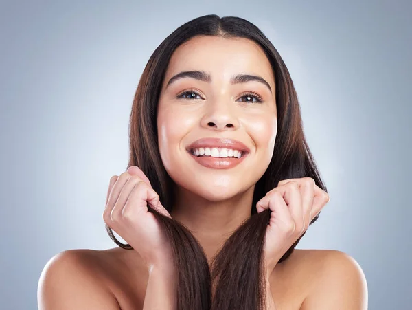 Portrait of a beautiful mixed race woman with clean skin and shiny smooth hair posing against a studio background. Woman holding her hair to show off healthy hair care.