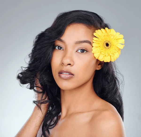 No beauty shines the way natural does. Studio portrait of an attractive young woman posing with a yellow flower in her hair against a grey background