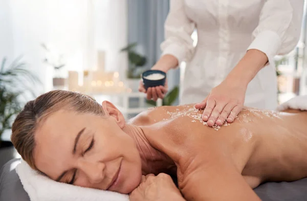 A body scrub will do you a world of good. a mature woman enjoying an exfoliating salt scrub massage at a spa