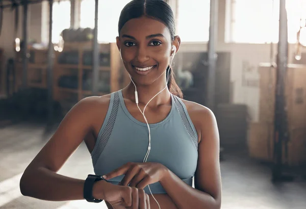 Real change takes time, so just be consistent. Portrait of a sporty young woman listening to music and checking her watch while exercising in a gym