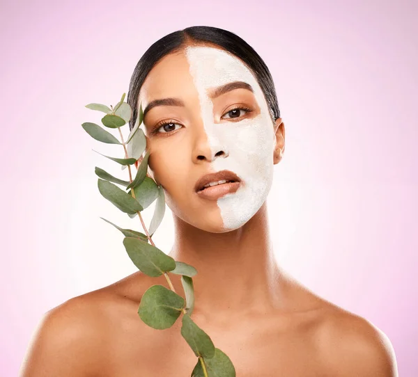Organic products are great for my skin. Studio shot of an attractive young woman holding a plant and having a facial against a pink background