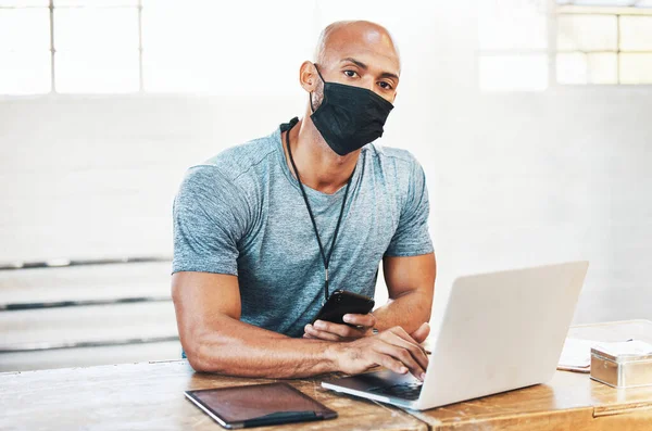 Lets continue to stay healthy in the safest way possible. Portrait of a muscular young man wearing a face mask and using a laptop while working in a gym
