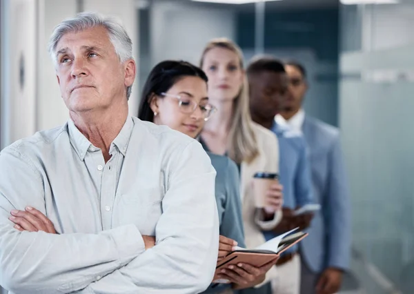 How much longer do I have to wait. a mature businessman standing with his arms crossed while waiting in line in an office