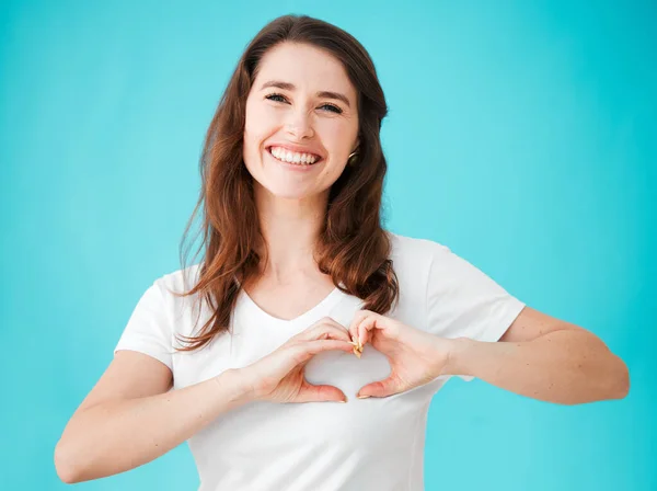 My heart is full of love. Studio portrait of an attractive young woman making a heart shape over her chest against a blue background