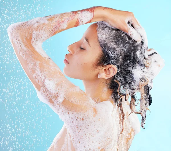 Feeling rejuvenated from head to toes. a woman washing her hair against a blue background