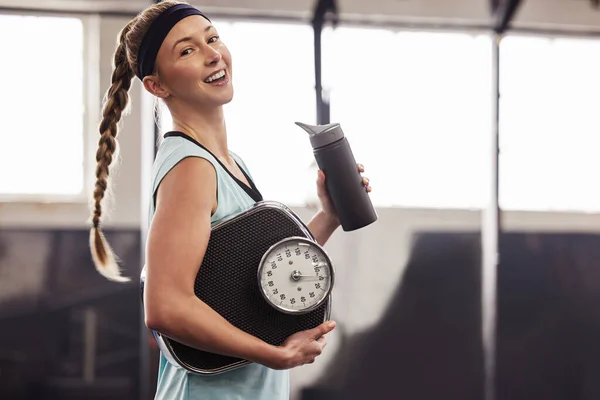 Healthier life Happier life. a young woman holding a water bottle and weighing scale at the gym