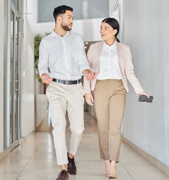 Doing their business on the move. Full length shot of two young businesspeople talking as they walk through a corridor in their office