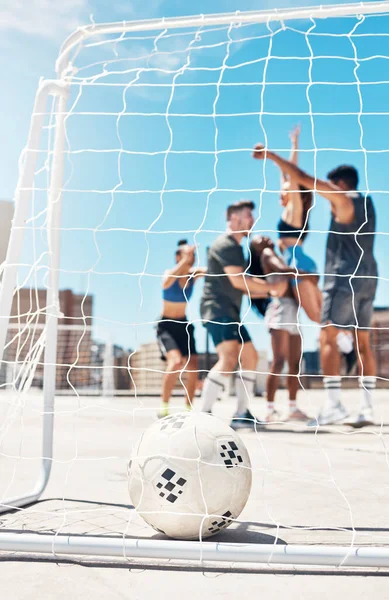 Football, soccer team and ball in goal post or net with diversity sports group of men and women in celebration of win, winning and scoring on urban rooftop. Exercise, concrete training and champions.