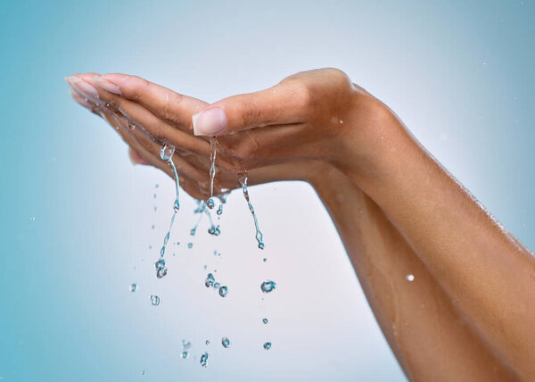 All about hydrating my skin. an unrecognisable woman cupping her hands to catch water against a blue background in the studio