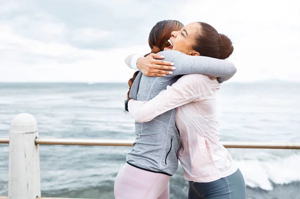 Fitness, friends and women hug at the ocean, success and workout goals, celebration of teamwork with personal trainer. Health, exercise and training target, happy woman hugging friend at sea waves