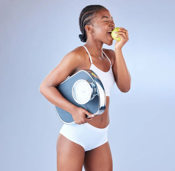 Want to reach that goal weight Eat right. Studio shot of a young woman eating an apple and holding weighing scale under her arm
