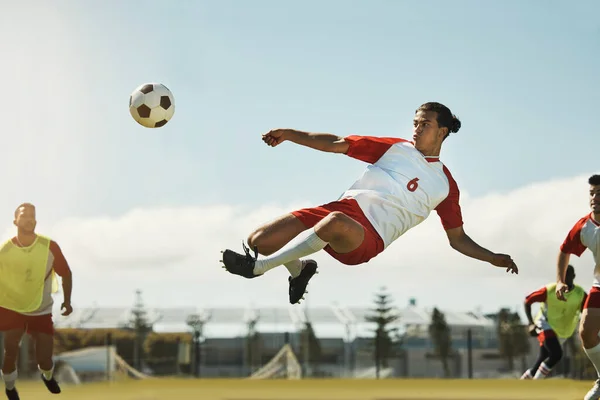 Soccer, game and man kicking a ball during training with the team on a field for sports. Athlete football player in the air to jump for a goal while playing in a professional match or competition.