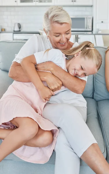 Grandmother, family and child at home with a senior woman having fun, bonding and laughing for tickle and playing on living room sofa. Grandma and girl grandchild spending time in Australia house.